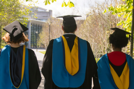 A photo of three UCD graduates walking through campus.